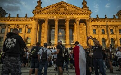 A demonstrator wrapped in a flag of the German empire stands opposite riot policemen standing guard in front of the Reichstag building, which houses the Bundestag lower house of parliament, after protesters tried to storm it at the end of a demonstration called by far-right and COVID-19 deniers to protest against restrictions, in Berlin, on August 29, 2020. (John MACDOUGALL / AFP)